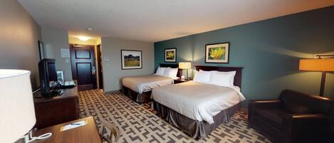 A hotel room with two beds, a desk with a lamp, a chair, and a TV.