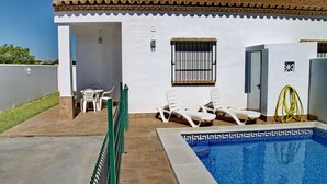 A white building with a tiled roof, a swimming pool with a decorative edge, and a small garden area with chairs. - Villa with private pool in rural area (CONIL DE LA FRONTERA)
