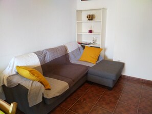 A living room with a grey sofa, a small ottoman, and a white shelf with decorative items. - Apartment with garage and shared pool (Chiclana de la Frontera)