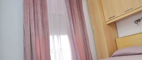 A bedroom with a bed, wooden wardrobe, and pink curtains.