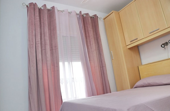 A bedroom with a bed, wooden wardrobe, and pink curtains. - Apartment for four in Cádiz city centre (CADIZ)