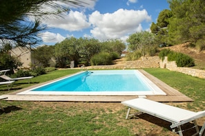 A rectangular swimming pool with a wooden deck, surrounded by a grassy lawn and trees.