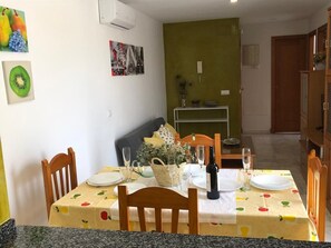 A dining area with a table set for four, chairs, a basket, a bottle of wine, and a white wall with artwork.