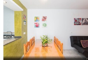 A dining area with a wooden table, chairs, a potted plant, and a black sofa.