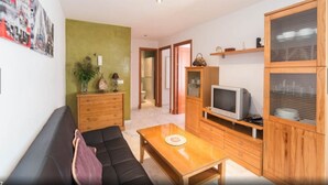 Un salon comprenant un canapé, une table basse, des meubles en bois, un téléviseur et une porte donnant sur une autre pièce.