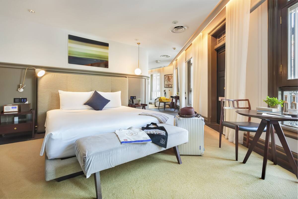 A hotel room with a large bed, bedside table, lamp, and a small table with chairs.