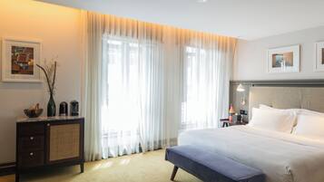 Una habitación de hotel con una cama grande, una mesita de noche con lámpara, una ventana con cortinas de encaje y un cuadro en la pared.