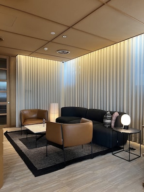 A modern living room with a black sofa, a brown leather chair, and a round table with a lamp.