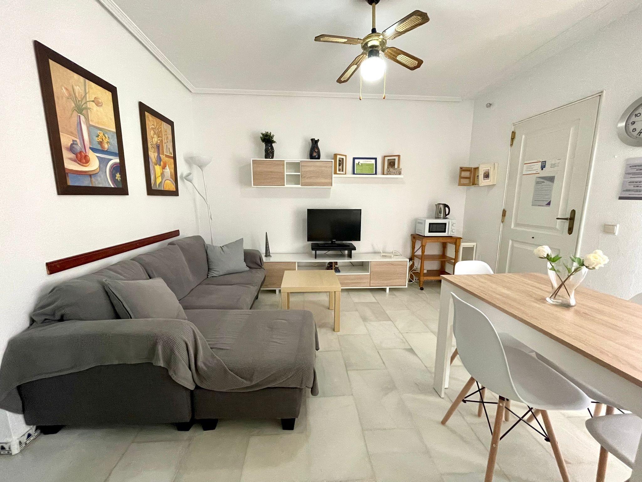 Een woonkamer met een bank, televisie, salontafel en een eethoek met stoelen.