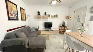 Una sala de estar con sofá, televisor, mesa de centro y comedor con sillas.