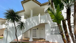 Un edificio blanco con un porche cubierto, una palmera y una ventana con rejas.