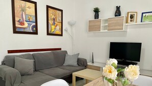 Una sala de estar con un sofá, un televisor, una mesa con un florero y dos cuadros en la pared.