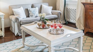 A cozy living room with a white table set with drinks and flowers, a grey sofa, and a wooden cabinet.