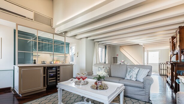 A spacious living area with a grey sofa, a white coffee table, and a kitchen area with a glass cabinet.