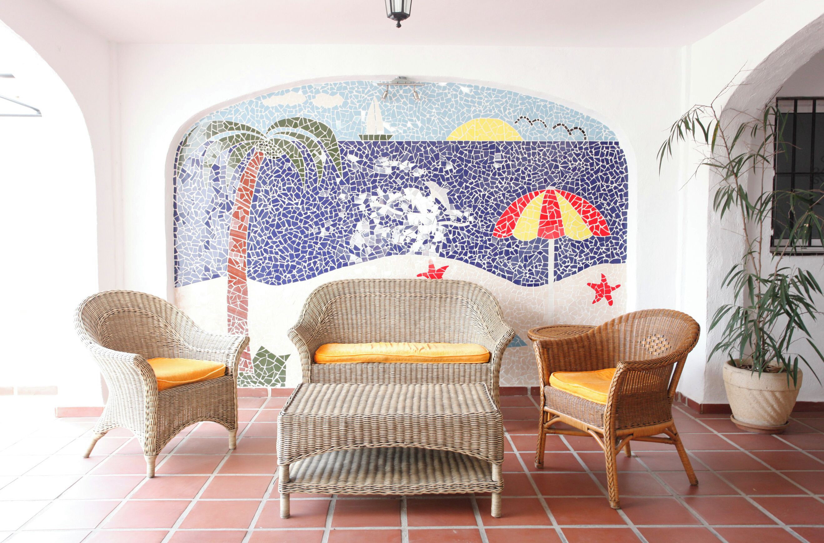 A room with a mosaic wall, wicker furniture, and a potted plant.