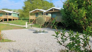 A row of wooden cabins with balconies, surrounded by gravel and greenery.