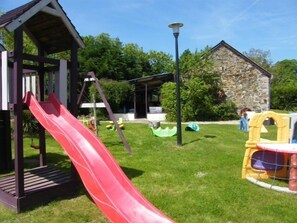 Ein Spielplatz mit einer roten Rutsche, einer Schaukel und einem kleinen Spielhäuschen.