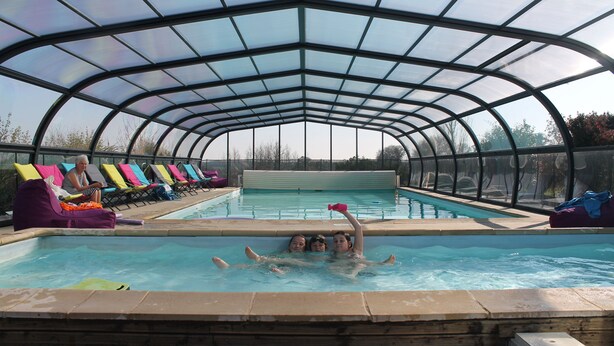 A covered swimming pool with lounge chairs and a hot tub area.