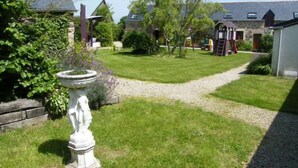 A well-maintained garden with a statue, a gravel path, and a building with a sloped roof.