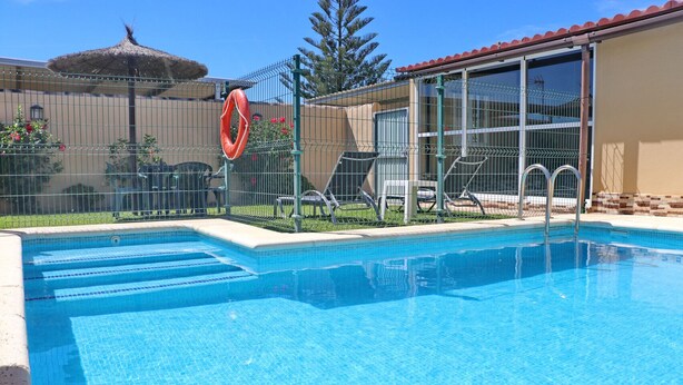 A clear blue pool with steps leading into it, surrounded by a fence and a building with large windows.