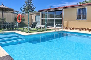 Une piscine à l’eau d’un bleu limpide, entourée d’une clôture, avec une chaise et un parasol installés pour se détendre.