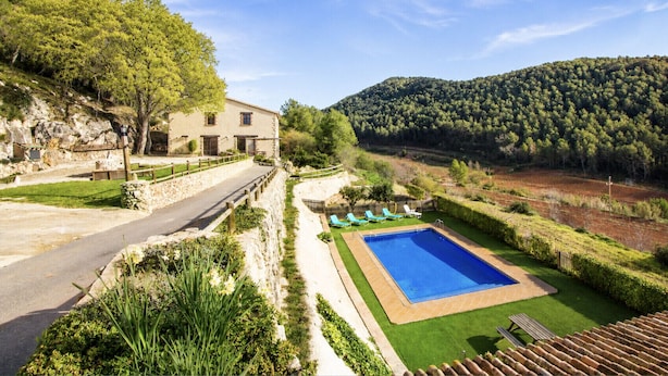 Une villa avec piscine, un chemin de pierre et une vue sur une colline boisée.