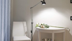 Una silla blanca, una mesa con una lámpara y un pequeño estante con un cuenco.