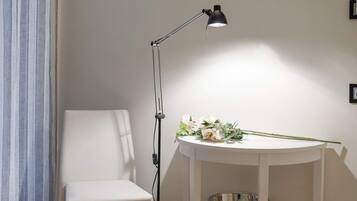 Una silla blanca, una mesa con una lámpara y un pequeño estante con un cuenco.