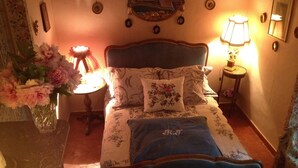A bedroom with a bed, floral bedding, a vase of flowers, a lamp, and a mirror on the wall.