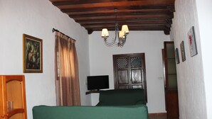 Una habitación con una cama, un televisor sobre un soporte, una puerta de madera y una araña.