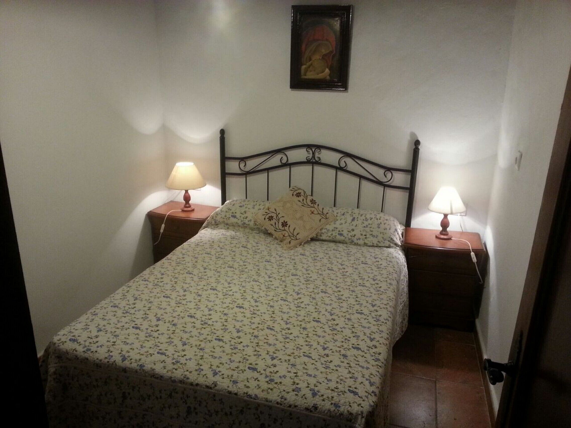 A bedroom with a bed, two bedside tables, two lamps, and a framed picture on the wall.