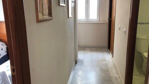 A narrow hallway with a tiled floor, wooden doors, and framed artwork on the walls.