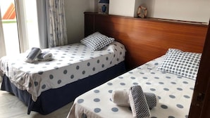 Two single beds with polka dot bedding, a wooden headboard, a small shelf with a lamp, and a clock on the wall.