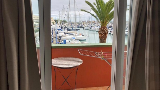 A balcony with a view of a marina, a palm tree, and a drying rack.