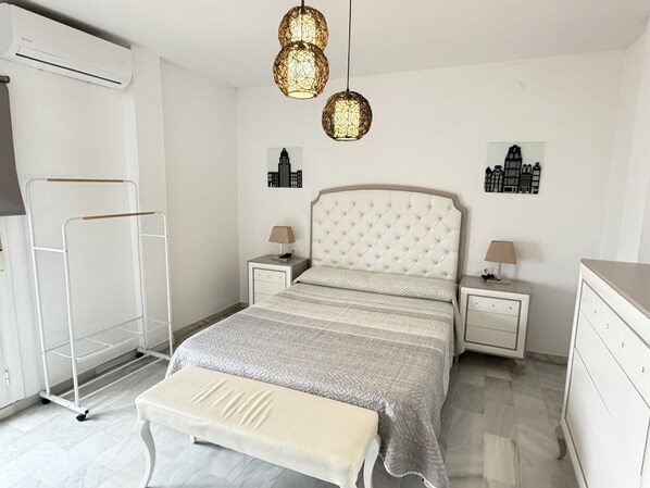 A modern bedroom with a bed, bedside tables, a hanging light fixture, and wall art. - Balcon Del Mar Primera Linea de Playa (Mijas)
