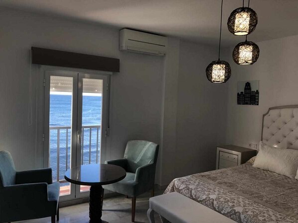 Une chambre d’hôtel avec un lit, une table, une chaise et un balcon donnant sur la mer.
