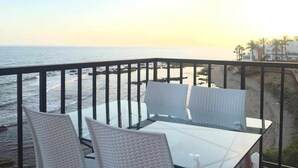 A balcony with a glass table and white chairs overlooking a beach and ocean. - Balcon Del Mar Primera Linea de Playa (Mijas)