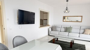 A modern living room with a flat-screen TV, a sofa, a glass coffee table, and a dining table with chairs. - Balcon Del Mar Primera Linea de Playa (Mijas)