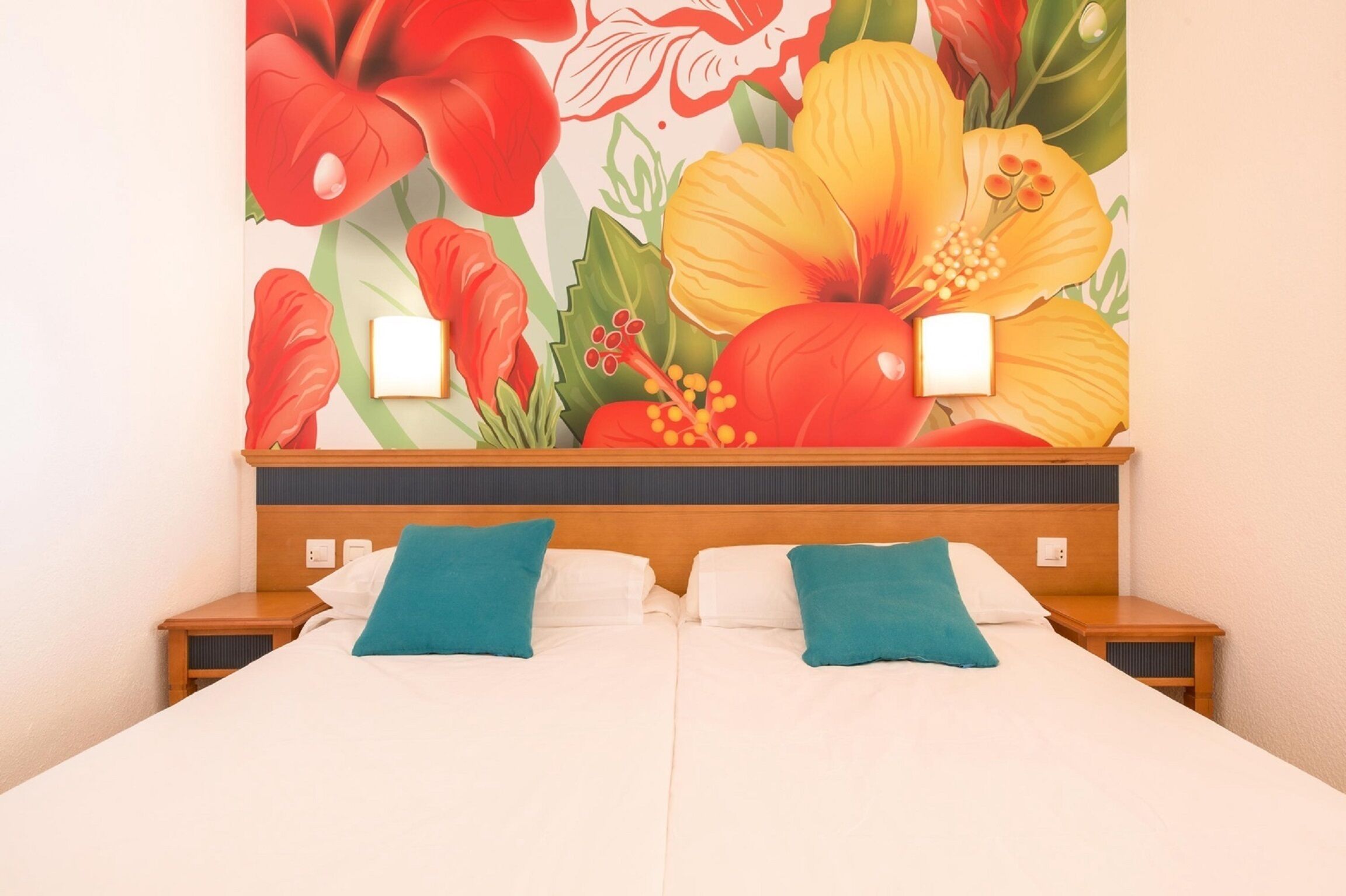 Una habitación de hotel con una cama, dos mesitas de noche y un gran mural floral en la pared.