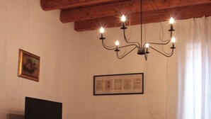 A living room with a wooden ceiling, a television on a stand, a sofa, a coffee table, and a chandelier. - FROM IRENE                                                           (Bassano del Grappa)