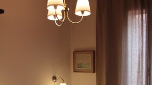 A neatly made bed with pillows, a wall-mounted lamp, and a framed picture on the wall. - FROM IRENE                                                           (Bassano del Grappa)