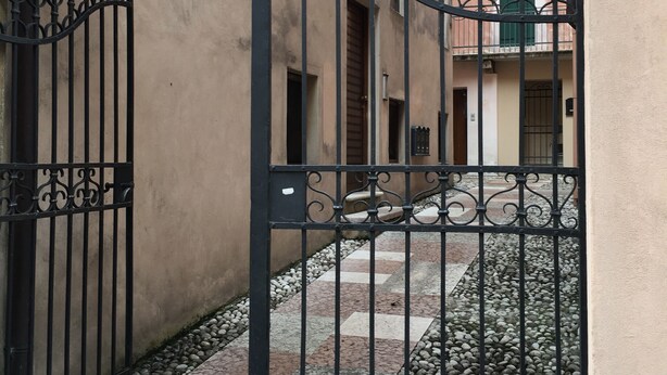A gated courtyard with a paved walkway and a building in the background. - FROM IRENE                                                           (Bassano del Grappa)