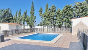 A rectangular swimming pool with a tiled deck surrounding it, enclosed by a wooden fence.