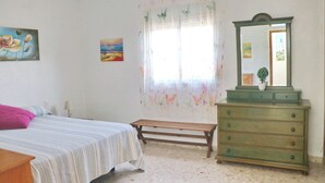 A bedroom with a bed, a dresser, a bench, and two paintings on the wall.