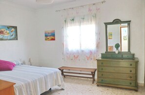 A bedroom with a bed, a dresser, a bench, and two paintings on the wall.
