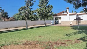 A grassy outdoor area with a white building, a paved walkway, and a parked car.