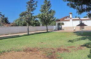 A grassy outdoor area with a white building, a paved walkway, and a parked car.