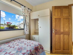 Quarto com cama, janela com cortinas, porta de madeira e guarda-roupa branco.