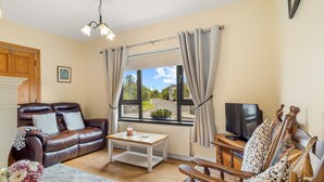 A living room with a leather sofa, a wooden coffee table, a TV, and a window with curtains. - Spiddal Cottage splendid base to tour the west (Spiddal)
