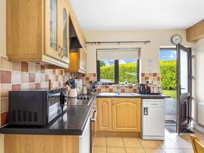 Une cuisine avec des meubles de rangement en bois, un micro-ondes noir, un évier et un lave-vaisselle.